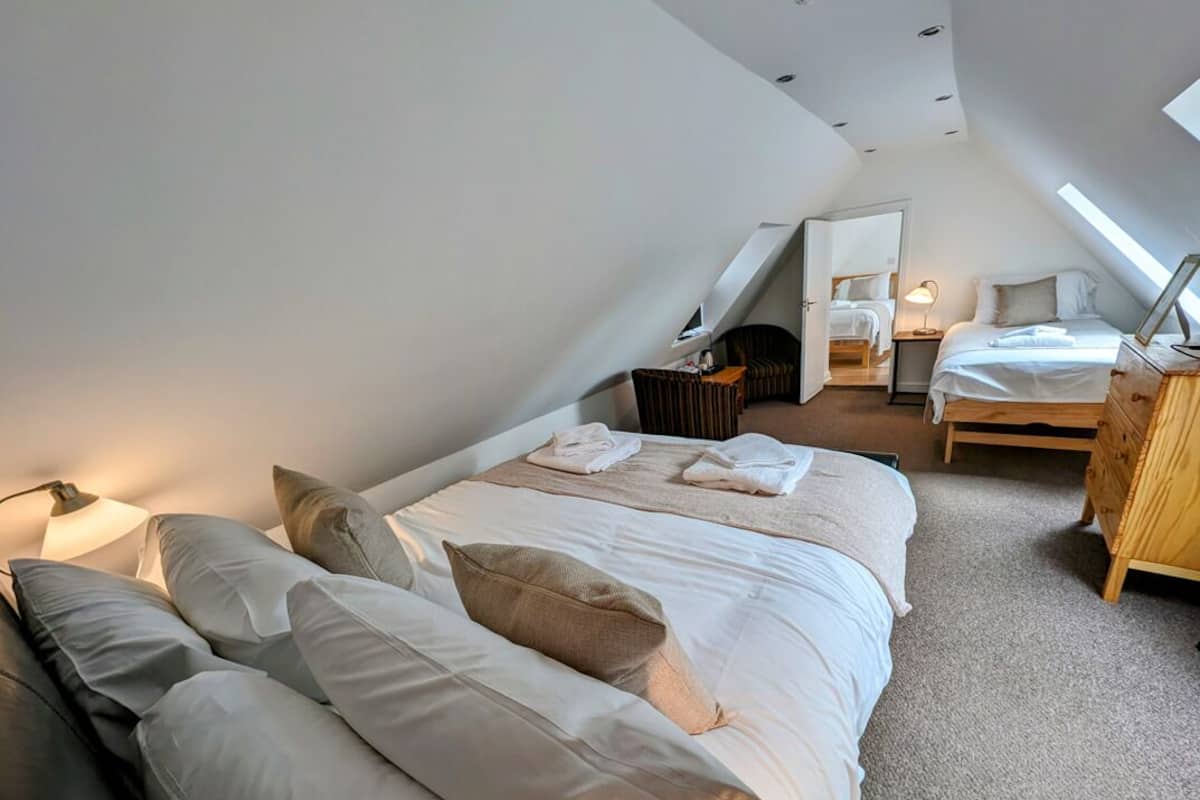 Quarto moderno e bem iluminado, com uma cama grande, mesa de cabeceira de madeira e uma escrivaninha com cadeira.