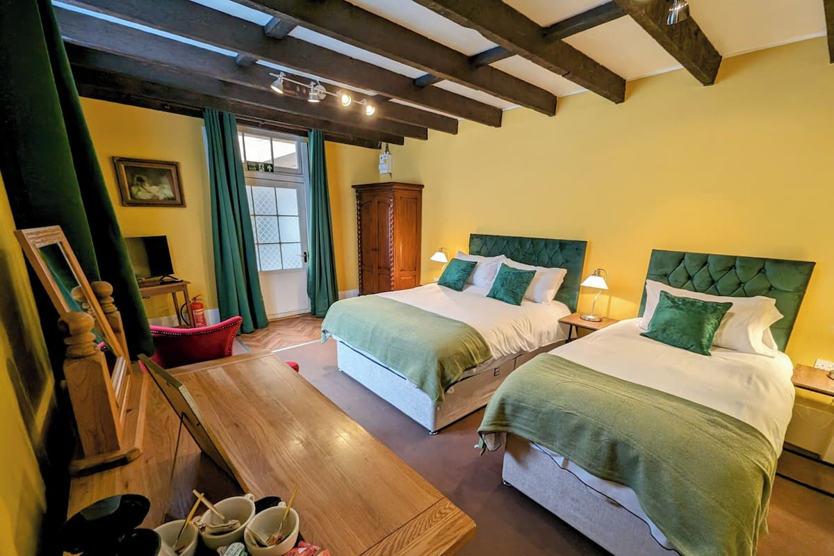Quarto de hotel com duas camas, mobiliário de madeira, teto de madeira e uma janela com cortinas.