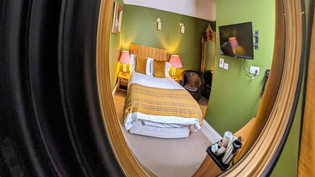 A hotel room with a bed, two bedside lamps, a television, and a chair. - Archway Guesthouse (Grantham)