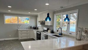 A modern kitchen with white cabinetry, a large island with bar stools, and blue pendant lights. - Beautiful house on the lake (Coventry)