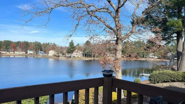A lakeside deck with a table and chairs, overlooking a calm lake and houses in the background. - Beautiful house on the lake (Coventry)