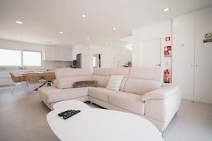 En moderne stue med en hjørnesofa, et spiseområde med bord og stole, og et køkken i baggrunden.