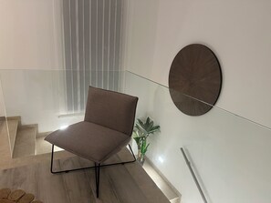 A modern interior with a glass railing, a brown chair, a potted plant, and a wall-mounted decorative piece.