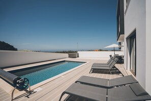 A rooftop pool with lounge chairs and a view of the ocean.