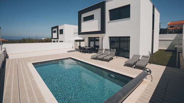 Une maison moderne à deux étages, dotée d’une piscine, d’un espace salon extérieur et offrant une vue sur l’océan.