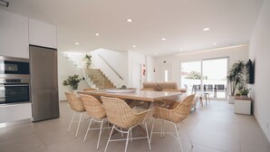 Une cuisine moderne dotée d’appareils électroménagers intégrés, un coin repas avec des chaises en osier et un escalier menant à un niveau supérieur.