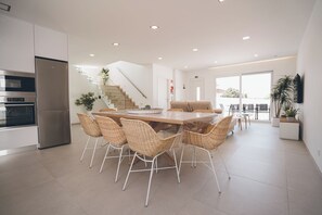 A modern kitchen with built-in appliances, a dining area with wicker chairs, and a staircase leading to an upper level.