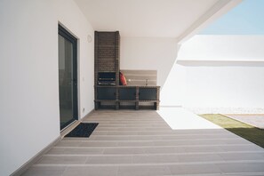 A modern outdoor patio with a built-in grill, a sliding glass door, and a small seating area.
