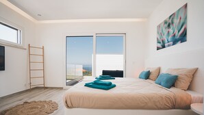 Une chambre à coucher moderne avec un grand lit, une vue sur l’extérieur grâce à une porte coulissante et un tableau accroché au mur.