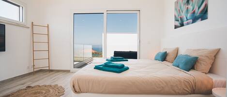 Un dormitorio moderno con una cama grande, vistas a través de una puerta corredera y un cuadro en la pared.