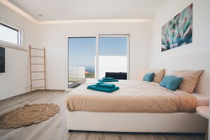 A modern bedroom with a large bed, a view through a sliding door, and a painting on the wall.