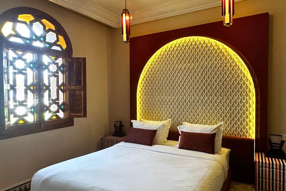 A hotel room with a bed, a decorative wall, and a window with stained glass.