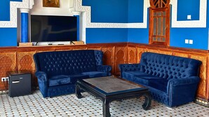 En stue med blå sofaer, et fjernsyn og detaljeret vægudsmykning.