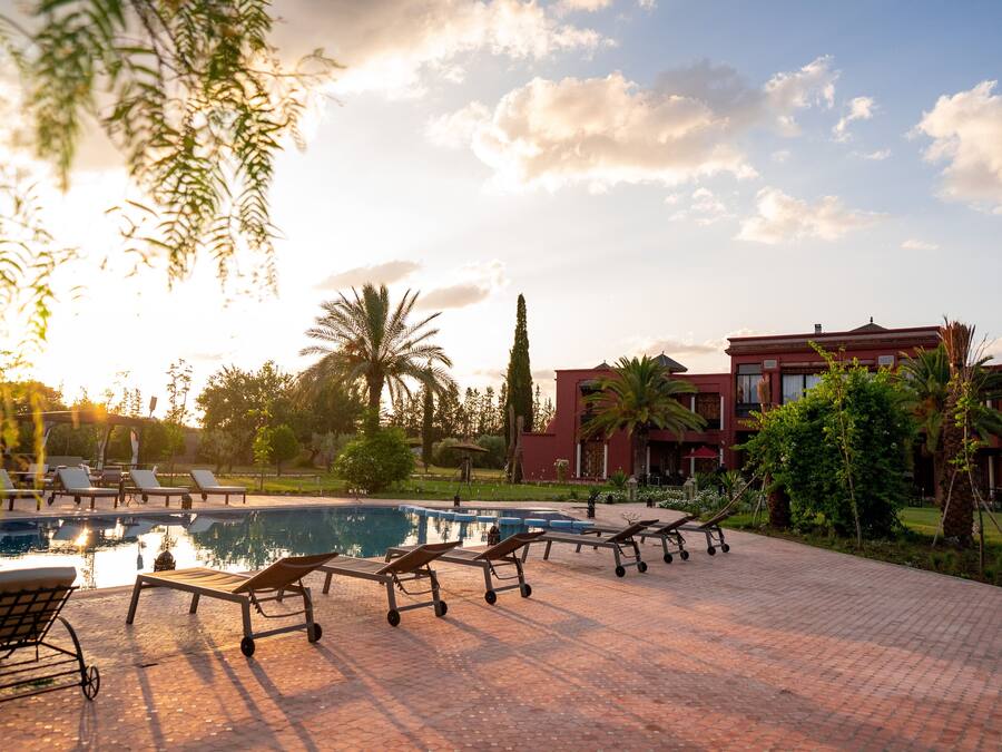 Zona de piscina con sillones de descanso y un edificio al fondo.