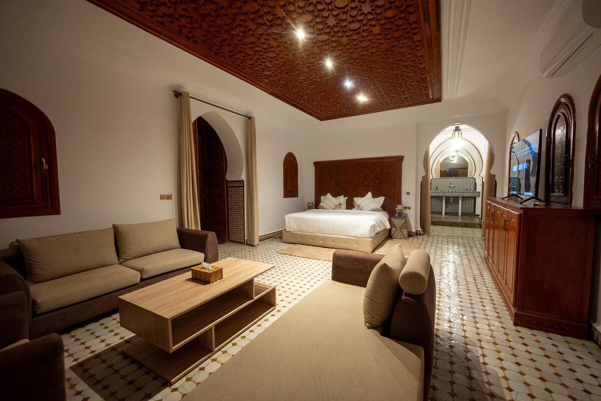 A spacious room with a large bed, a sofa, a wooden coffee table, and a patterned floor.