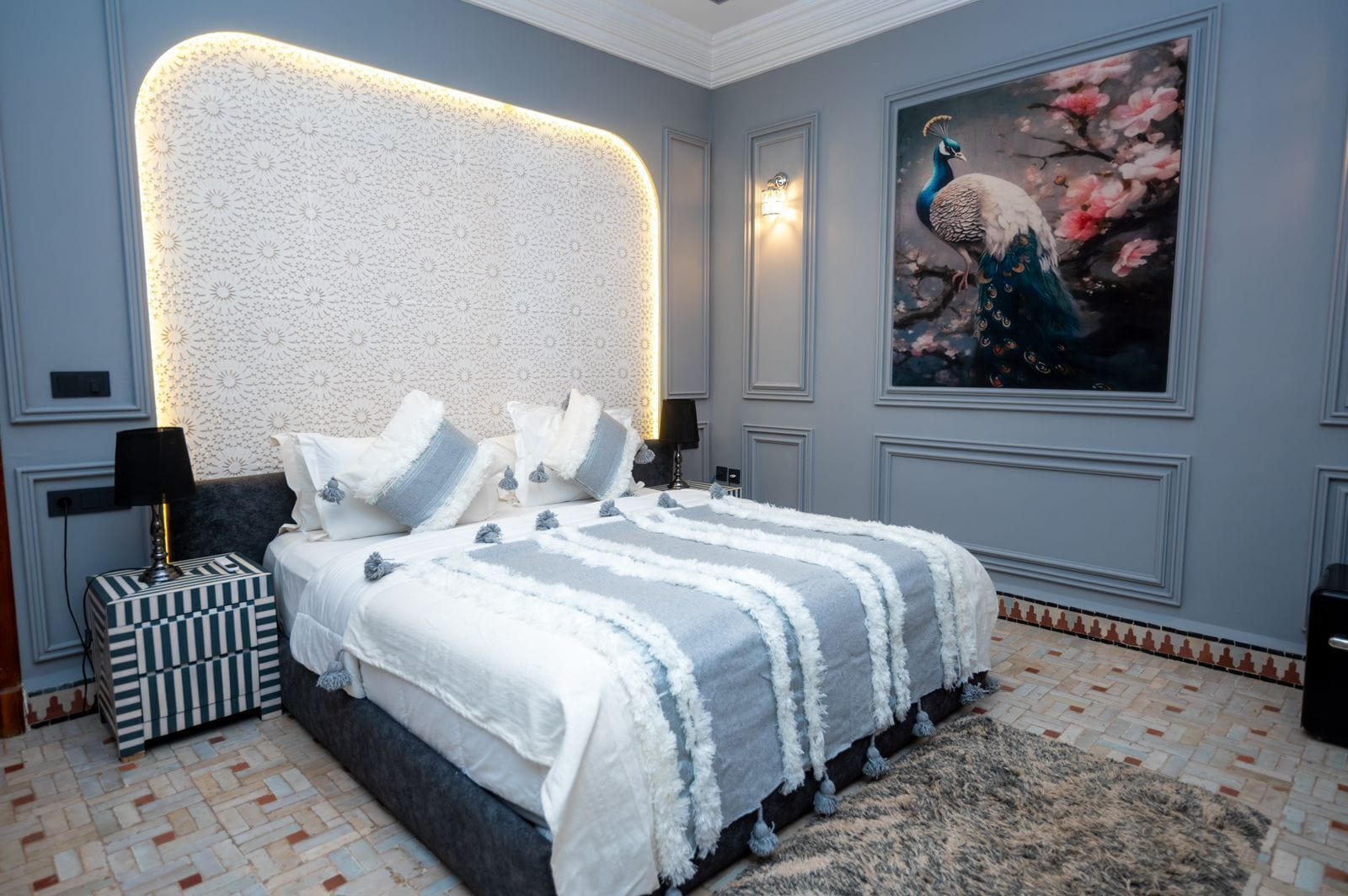 A bedroom with a large bed, a decorative headboard, a peacock painting, and a patterned floor.