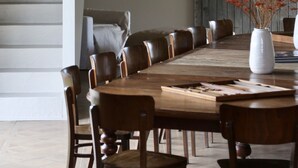 Un comedor con una gran mesa de madera rodeada de sillas, un jarrón con flores rojas y una puerta de madera rústica al fondo.