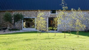 Un edificio de piedra con techo metálico, amplias ventanas y un césped con árboles.