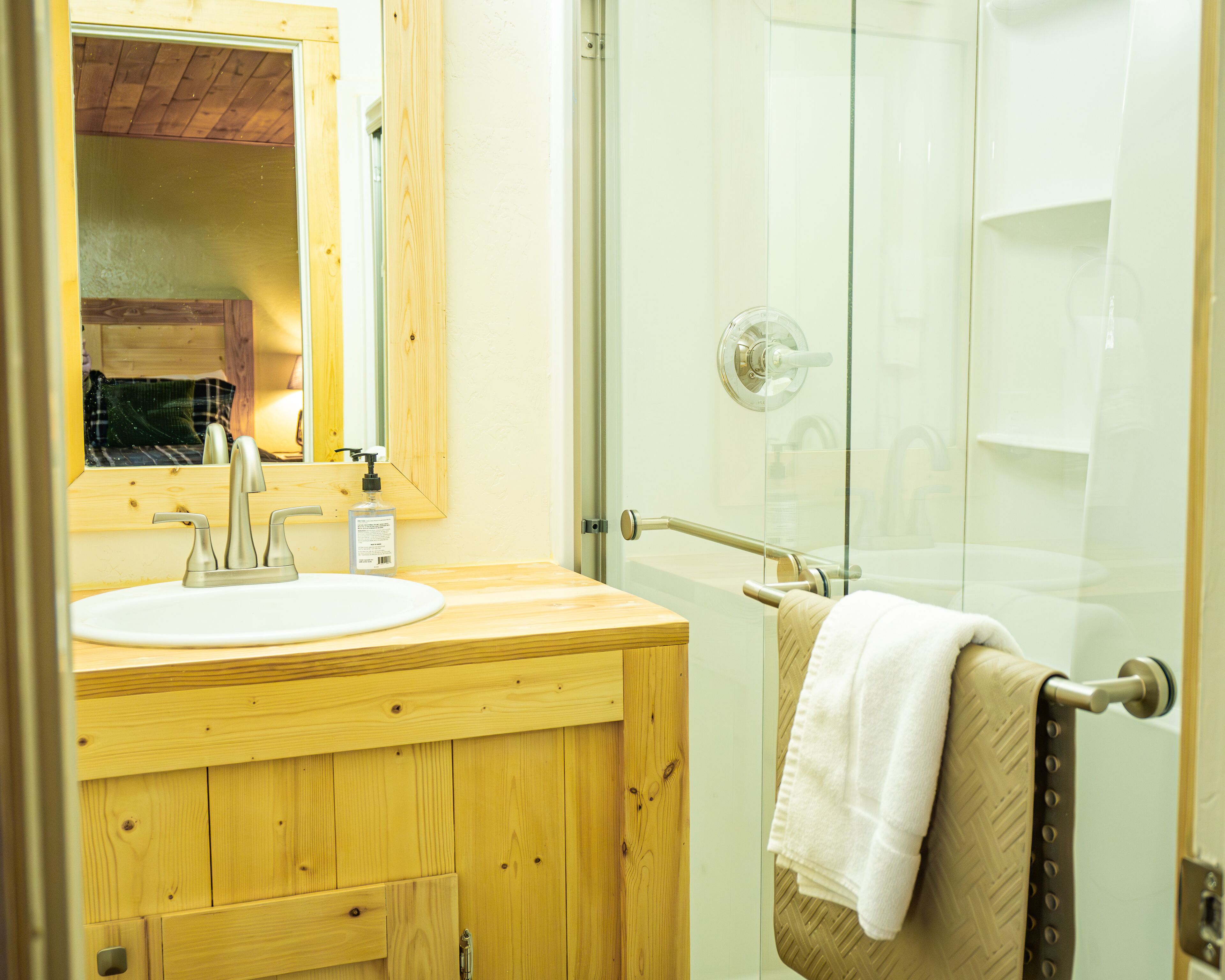 Une salle de bain avec un meuble-lavabo en bois, un lavabo blanc, un miroir et une cabine de douche en verre.