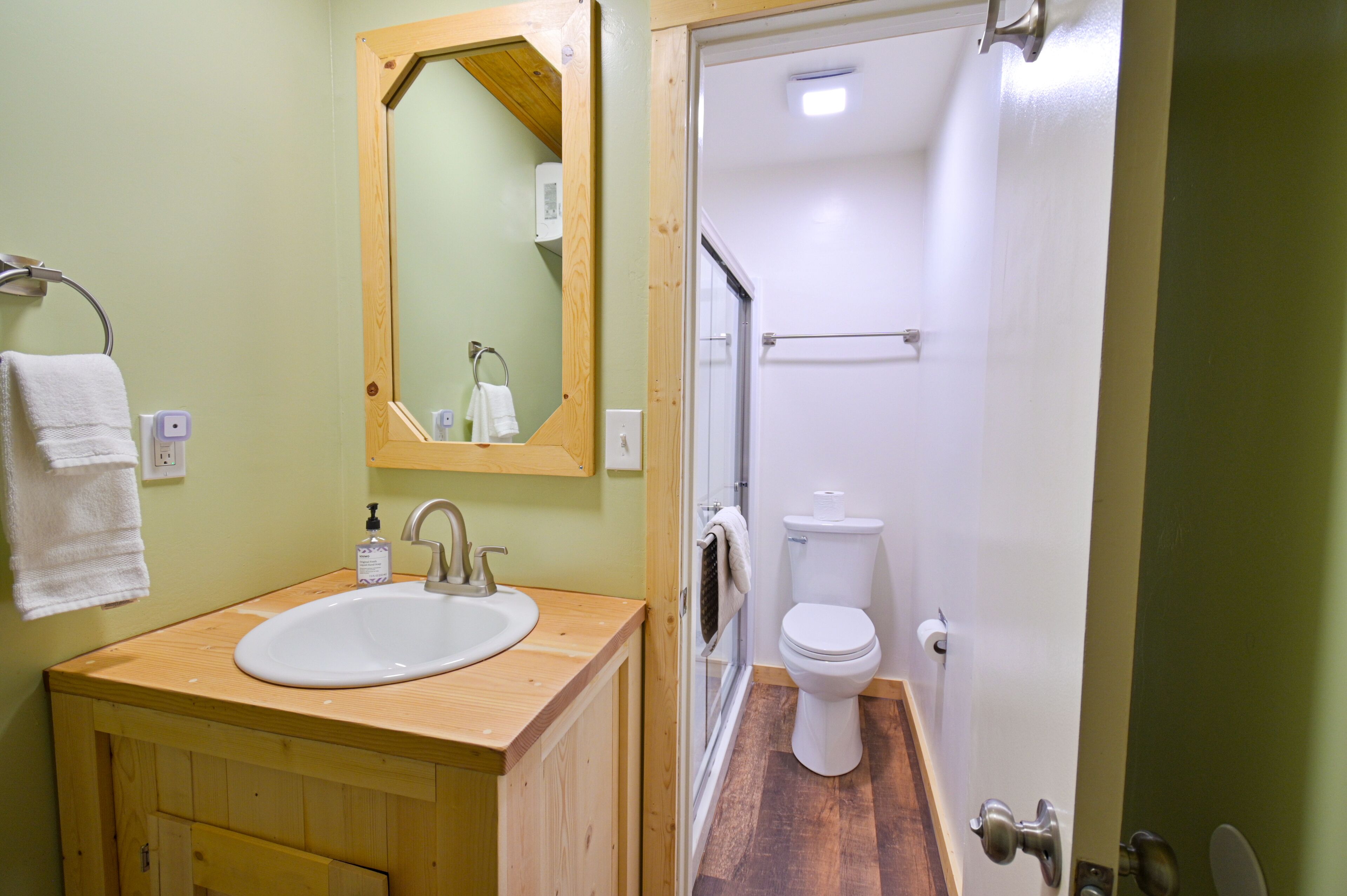 A bathroom with a wooden vanity, a white sink, a mirror, and a toilet.
