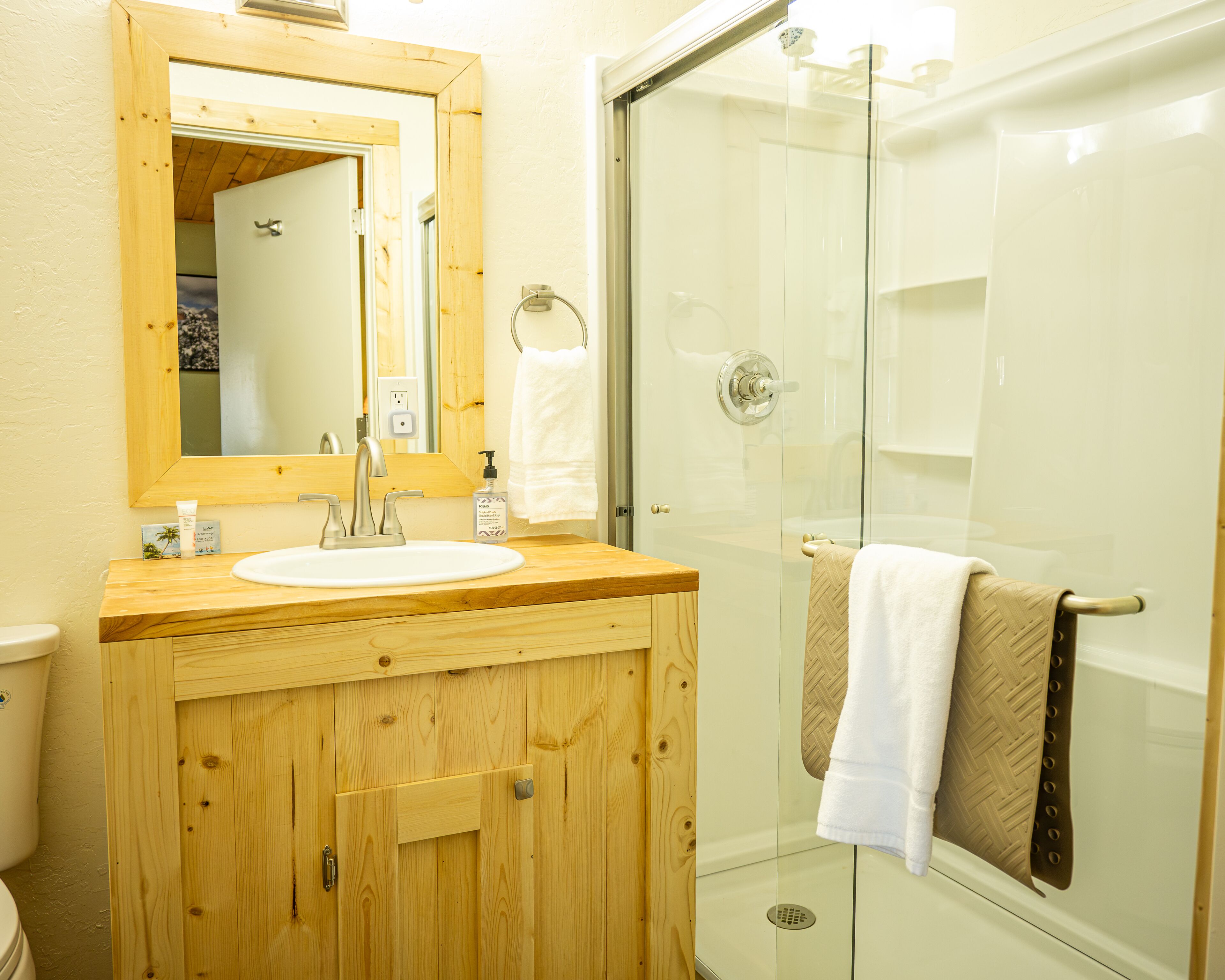 Un baño con tocador de madera, un lavabo, un espejo y cabina de ducha con mampara de vidrio.