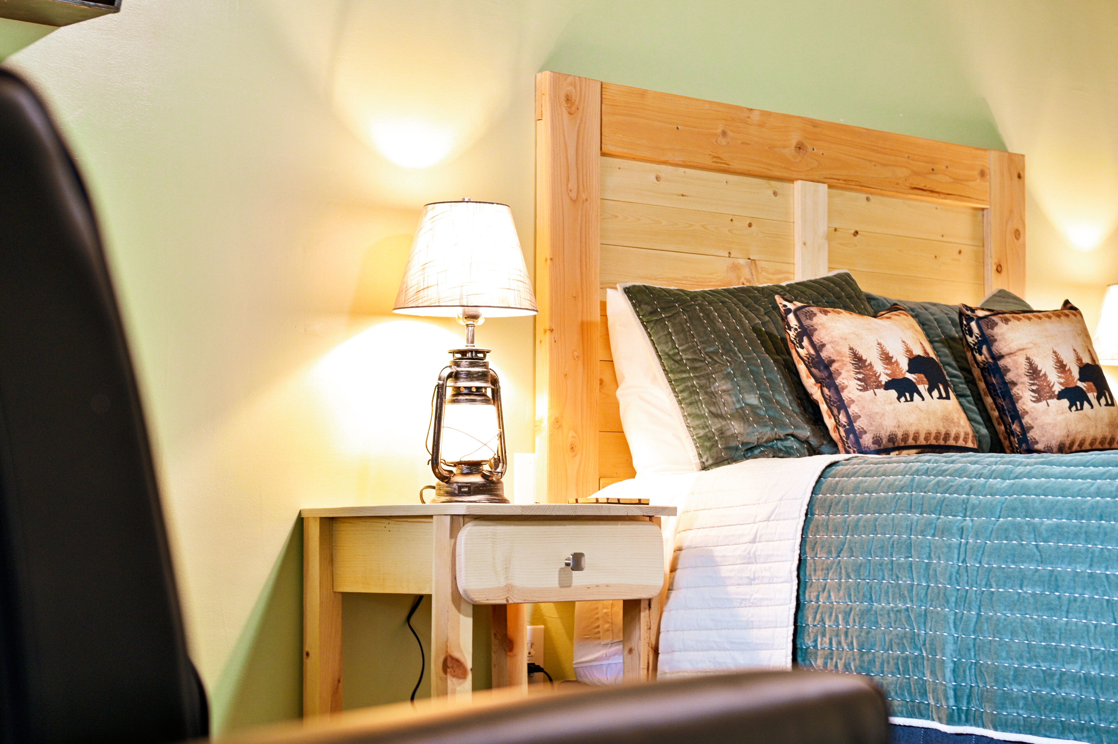 A bedroom with a wooden headboard, a bedside table with a lamp, a bed with a quilt and two decorative pillows.
