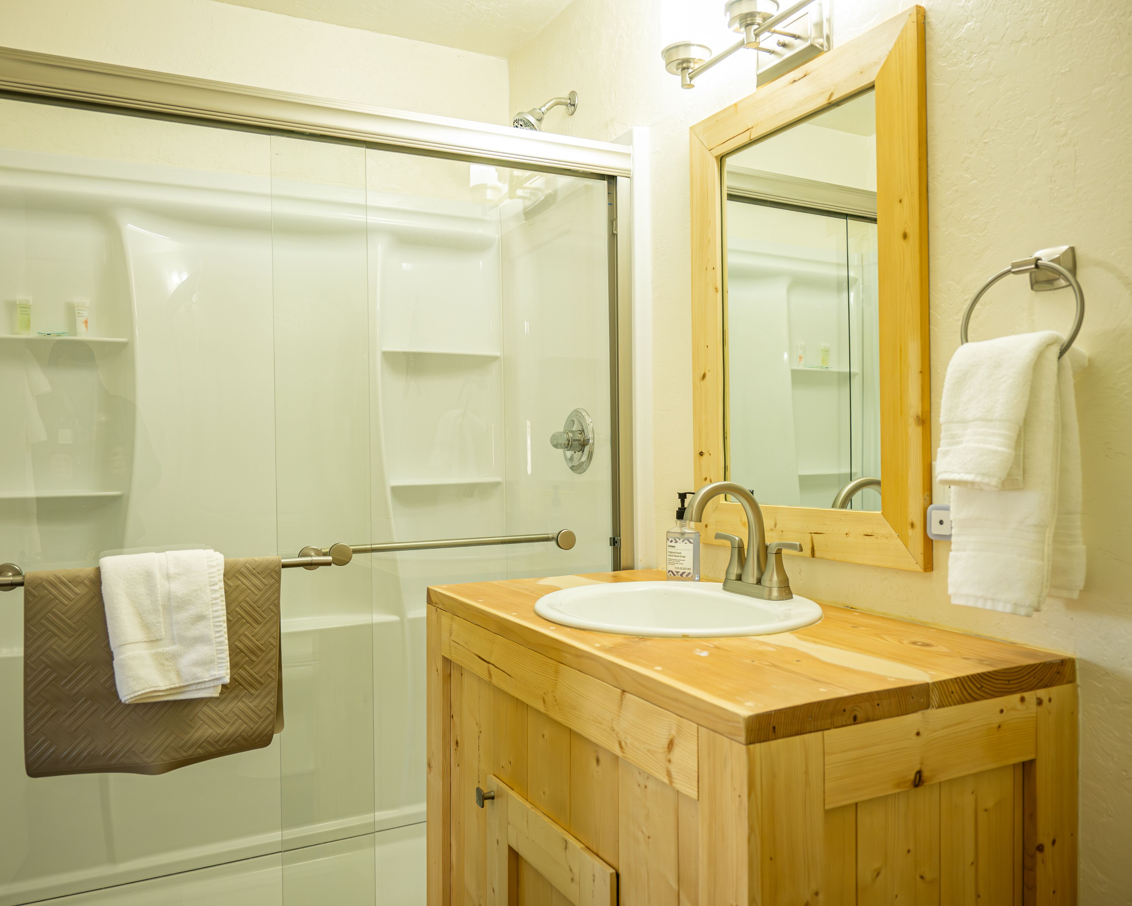 A bathroom with a glass shower enclosure, a wooden vanity with a sink, and a mirror.