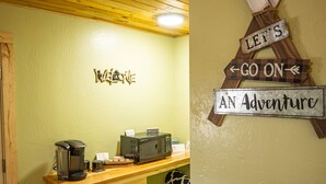 Una zona de cocina con mostrador de madera, cafetera y refrigerador. En la pared hay letreros que dicen 