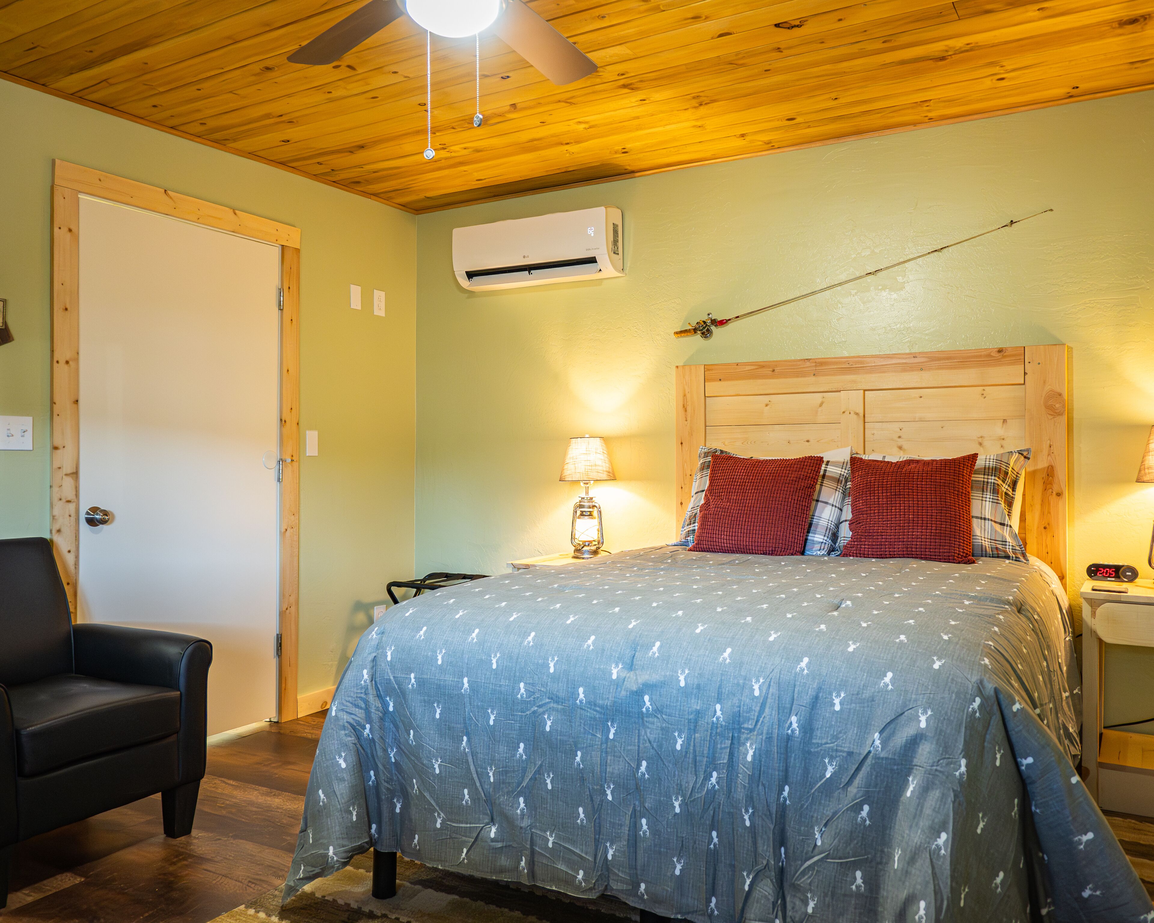 A bedroom with a bed, a chair, a nightstand, a lamp, an air conditioner, and a ceiling fan.