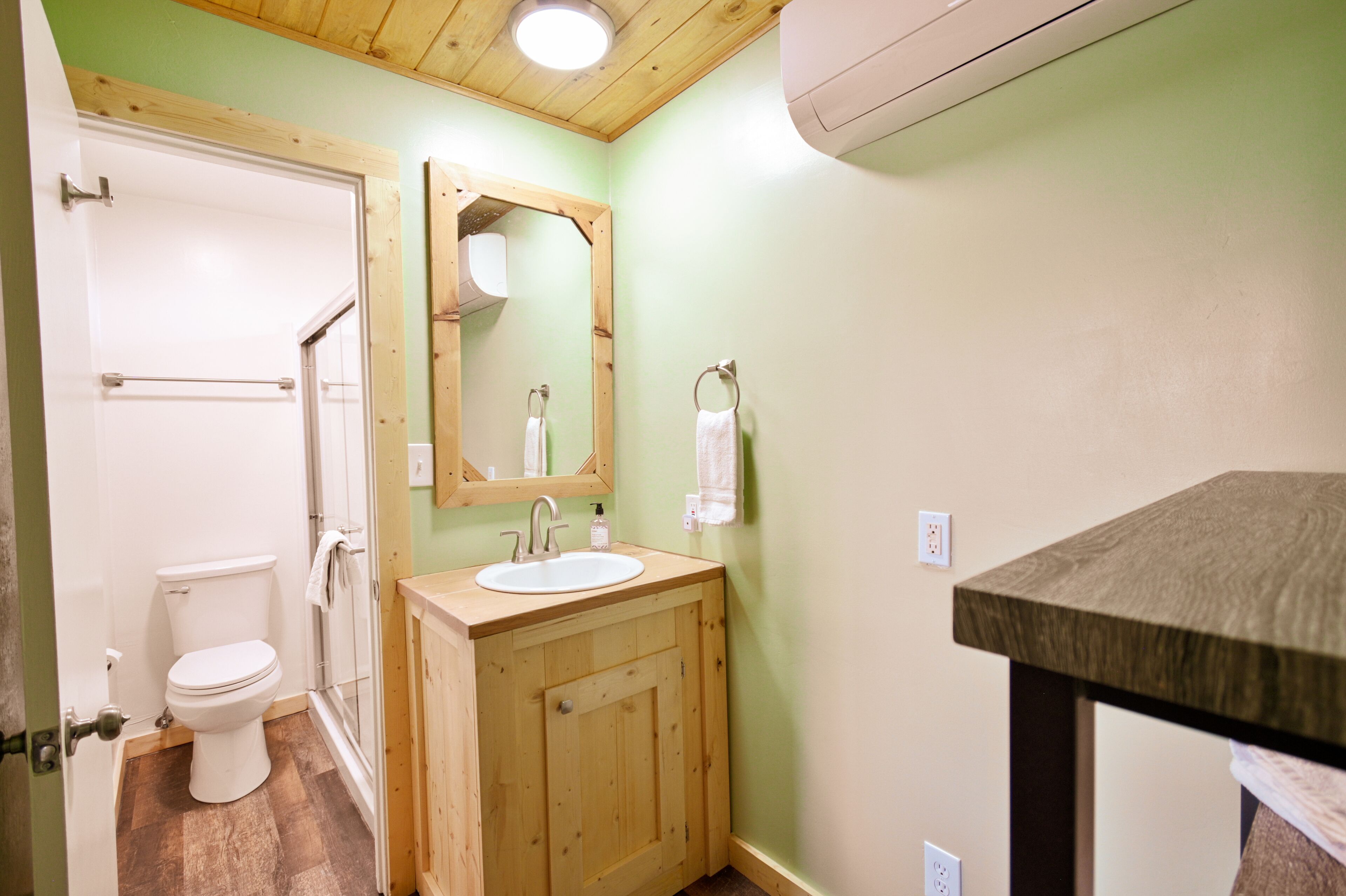 Un baño con tocador de madera, inodoro blanco y espejo sobre el lavamanos.