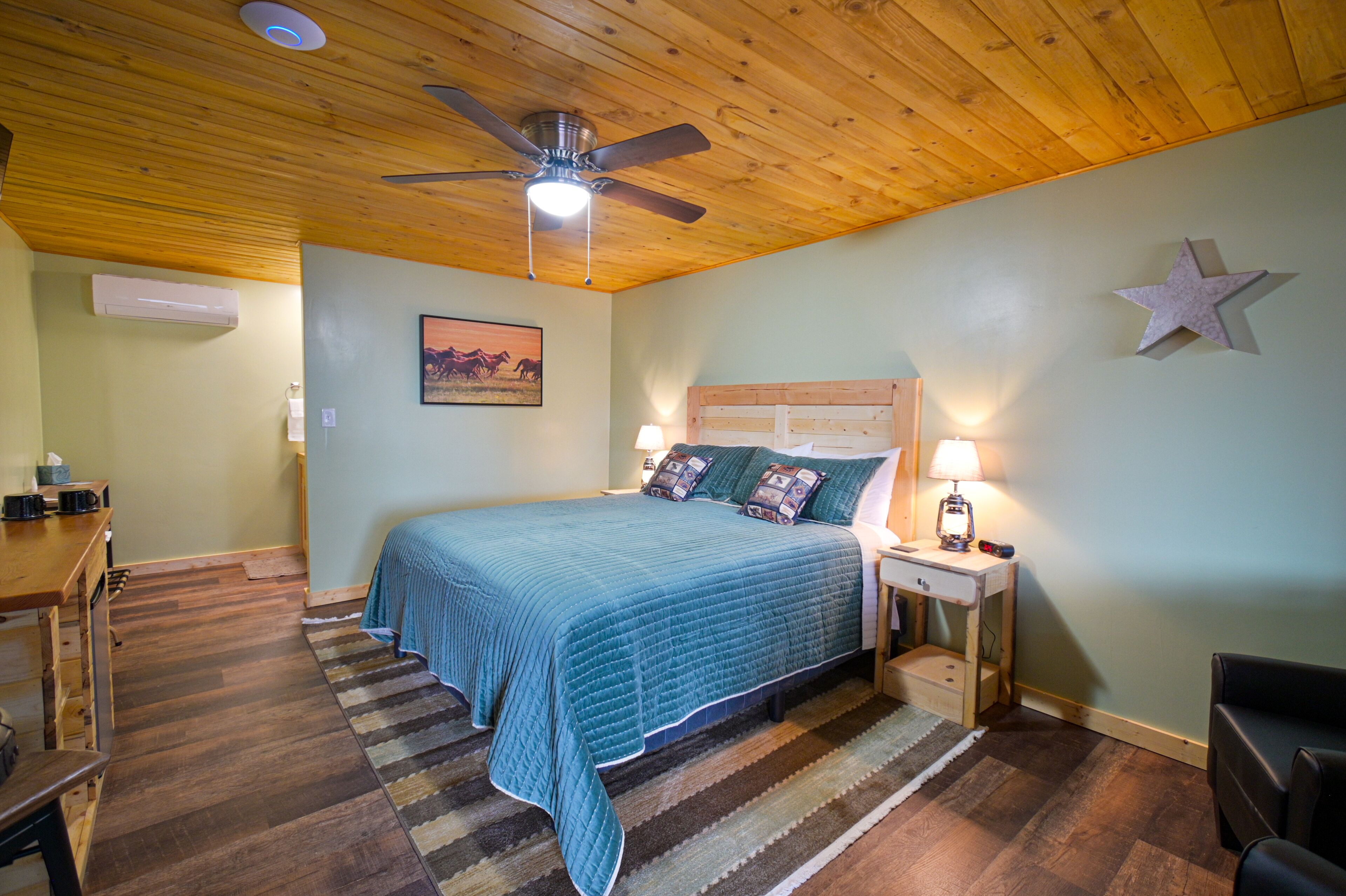 Un dormitorio con techo de madera, una cama con colcha azul, un escritorio con lámpara y un adorno con forma de estrella en la pared.