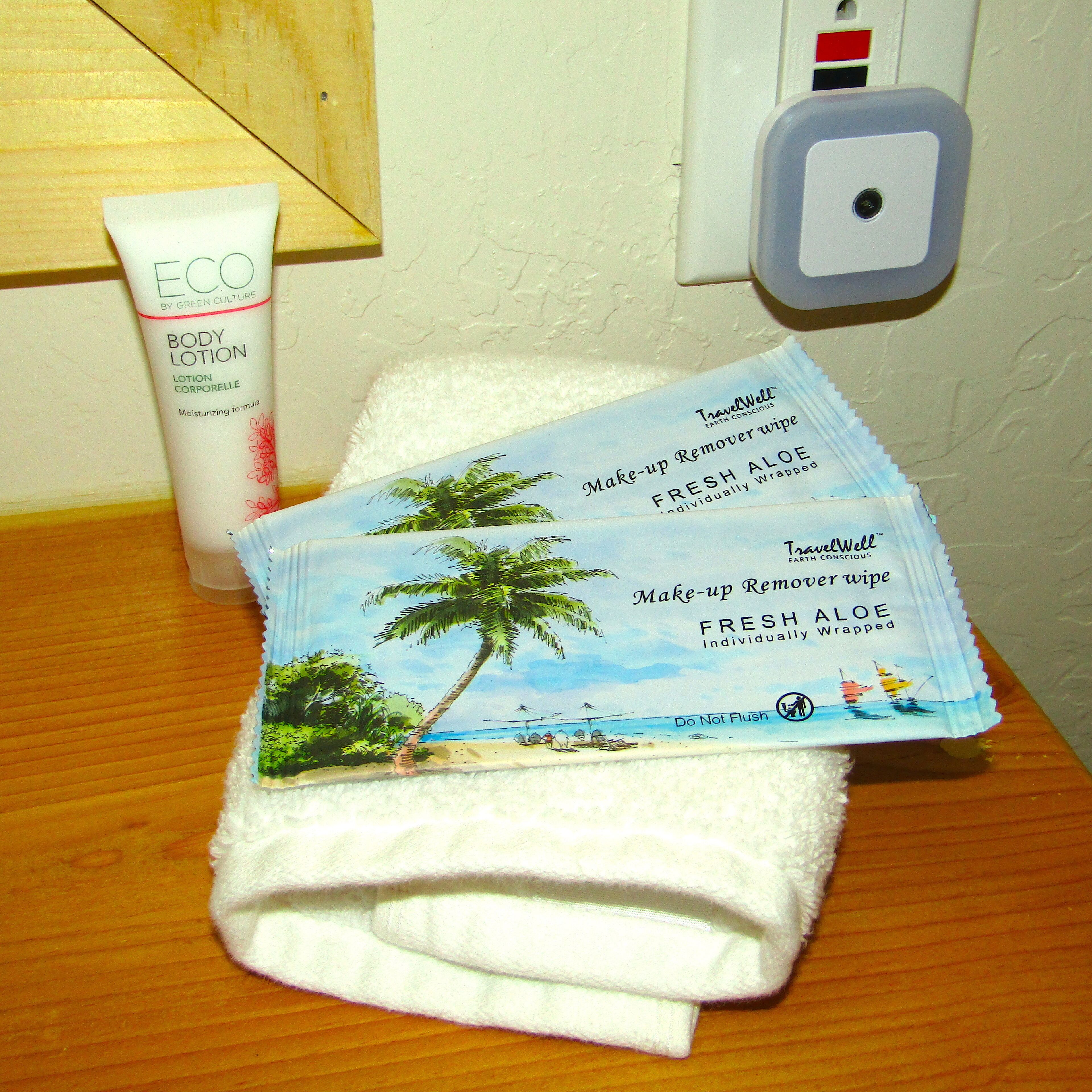 Een badkamer met een witte handdoek, een fles ECO bodylotion en een TravelWell make-up remoevedopje op een houten oppervlak.