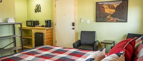 A room with a bed, a desk with a computer, an air conditioner, a chair, and a painting of a canyon.
