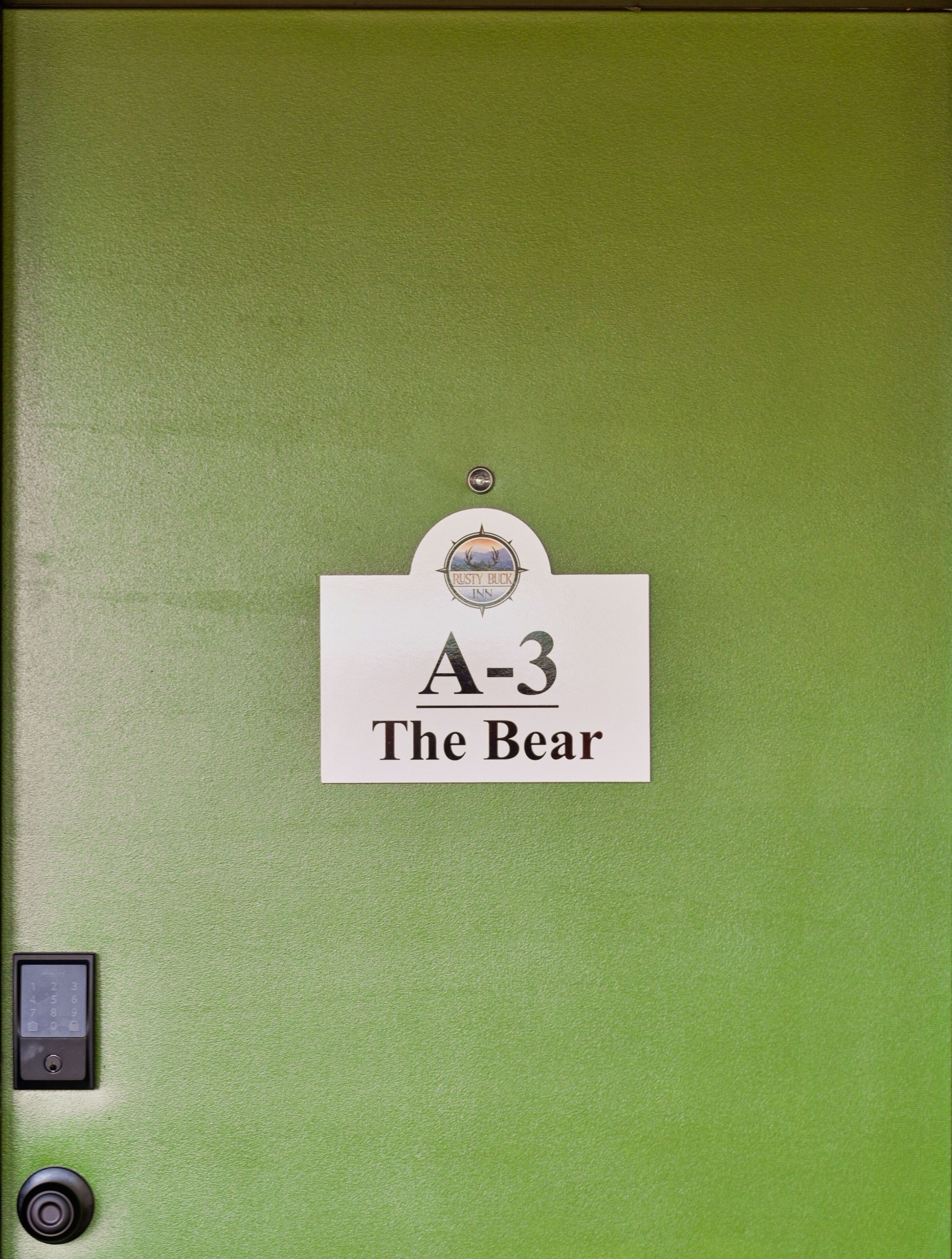 A green door with a sign reading "A-3 The Bear" and a logo above it.