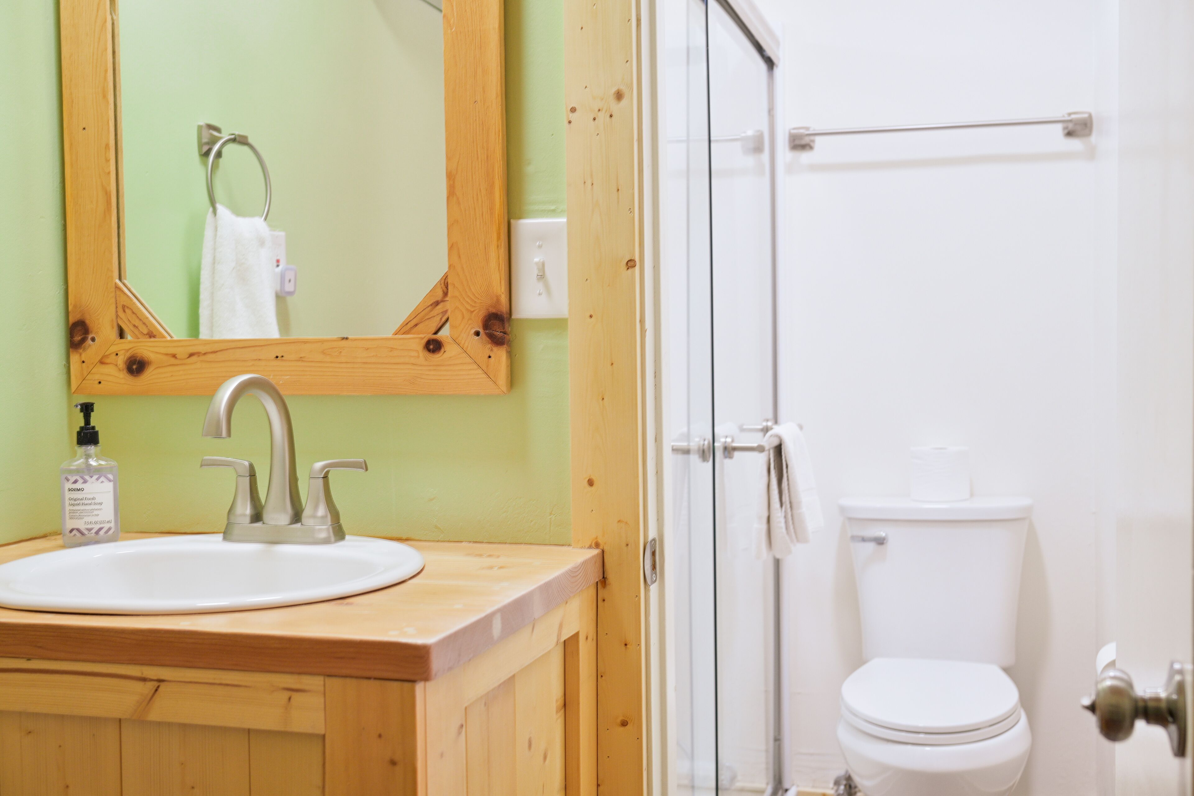 A bathroom with a wooden vanity, a sink, a mirror, a toilet, and a glass shower enclosure.