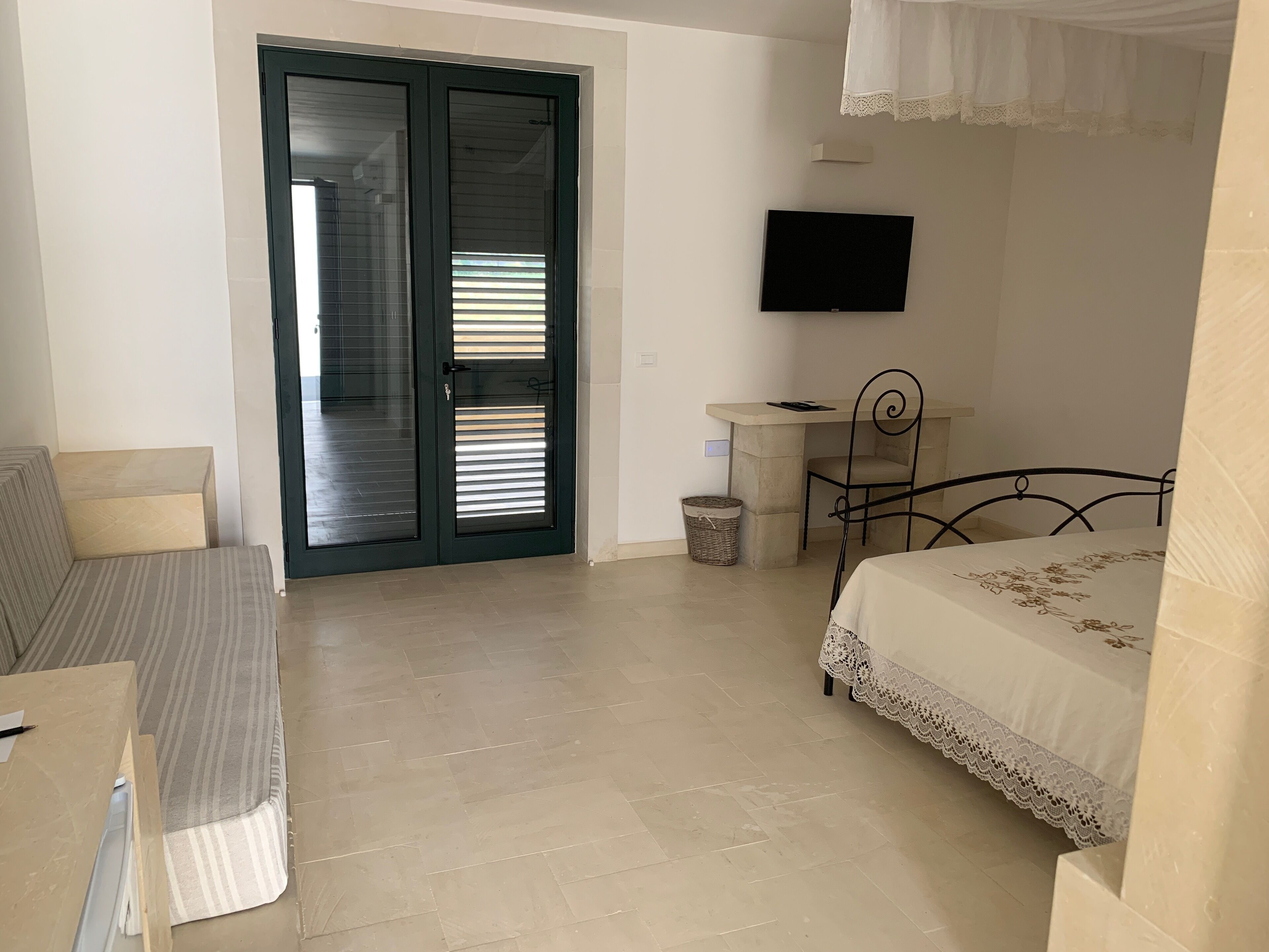 A bedroom with a bed, a desk, a chair, a television, and a sliding glass door.
