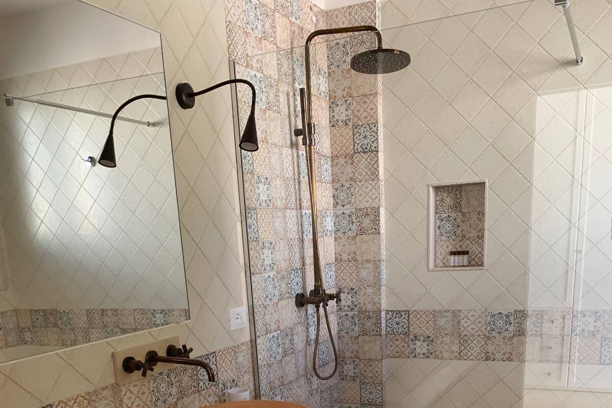 Un baño con dos lavamanos redondos, una ducha con cabezal de ducha manual y un espejo instalado en la pared.