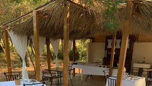 Una zona de menjador exterior amb taules preparades per a dues persones, cobertes amb tovallons blancs, i envoltades de cadires de fusta.