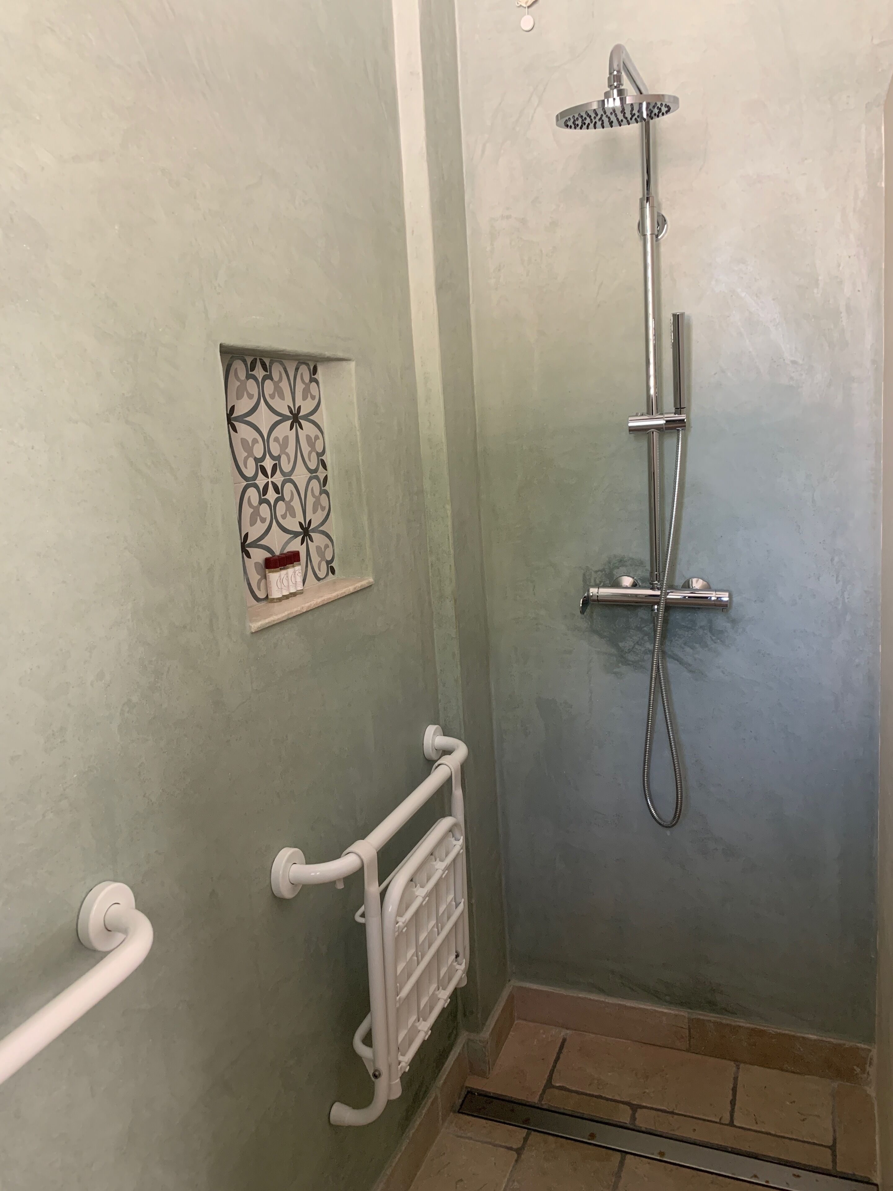 A bathroom with a shower, a towel rack, and a decorative tile design on the wall.