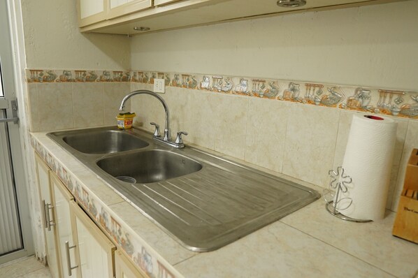 A kitchen with two stainless steel sinks, a paper towel holder, and a tiled backsplash with a decorative pattern.
