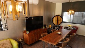 A modern living room with a wooden dining table, a flat-screen TV, and a large window with a view.
