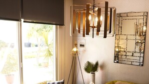 A green quilted sofa, a round table with a starfish and a bowl, a floor lamp, and a wall-mounted mirror.