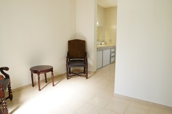 Un pasillo con una silla de madera y una mesita, que conduce a una zona de cocina con un lavamanos y alacenas.
