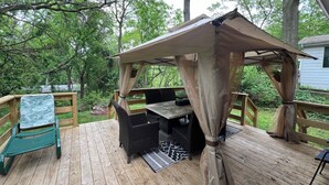 A wooden deck with a covered seating area, a table, and chairs.