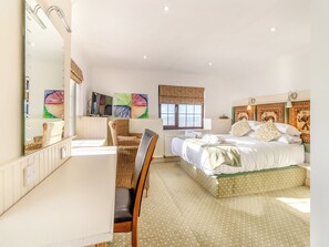 A bedroom with a large bed, a chair, a desk, a mirror, and artwork on the walls.