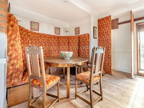 A dining area with a round table, two wooden chairs with cushioned seats, and a patterned curtain backdrop.