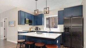 Een moderne keuken met donkerblauwe kastjes, een roestvrijstalen koelkast, een groot eiland met krukken en hanglampen.