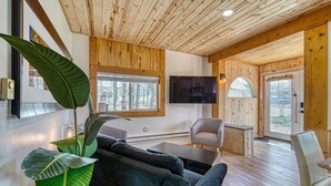 Ein gemütliches Wohnzimmer mit Holzbalkendecke, einem großen Fenster, einem Flachbildfernseher und einer bequemen Sitzecke.