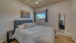 Ein Schlafzimmer mit einem Bett, einem Nachttisch, einem Fenster mit Blick auf ein Gebäude, einem Spiegel und einer Decke mit Holzbalken.