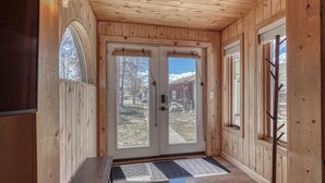 Ein Holzboden-Flur mit einer Doppeltür, die nach draußen führt, einer Bank und einer Fußmatte.